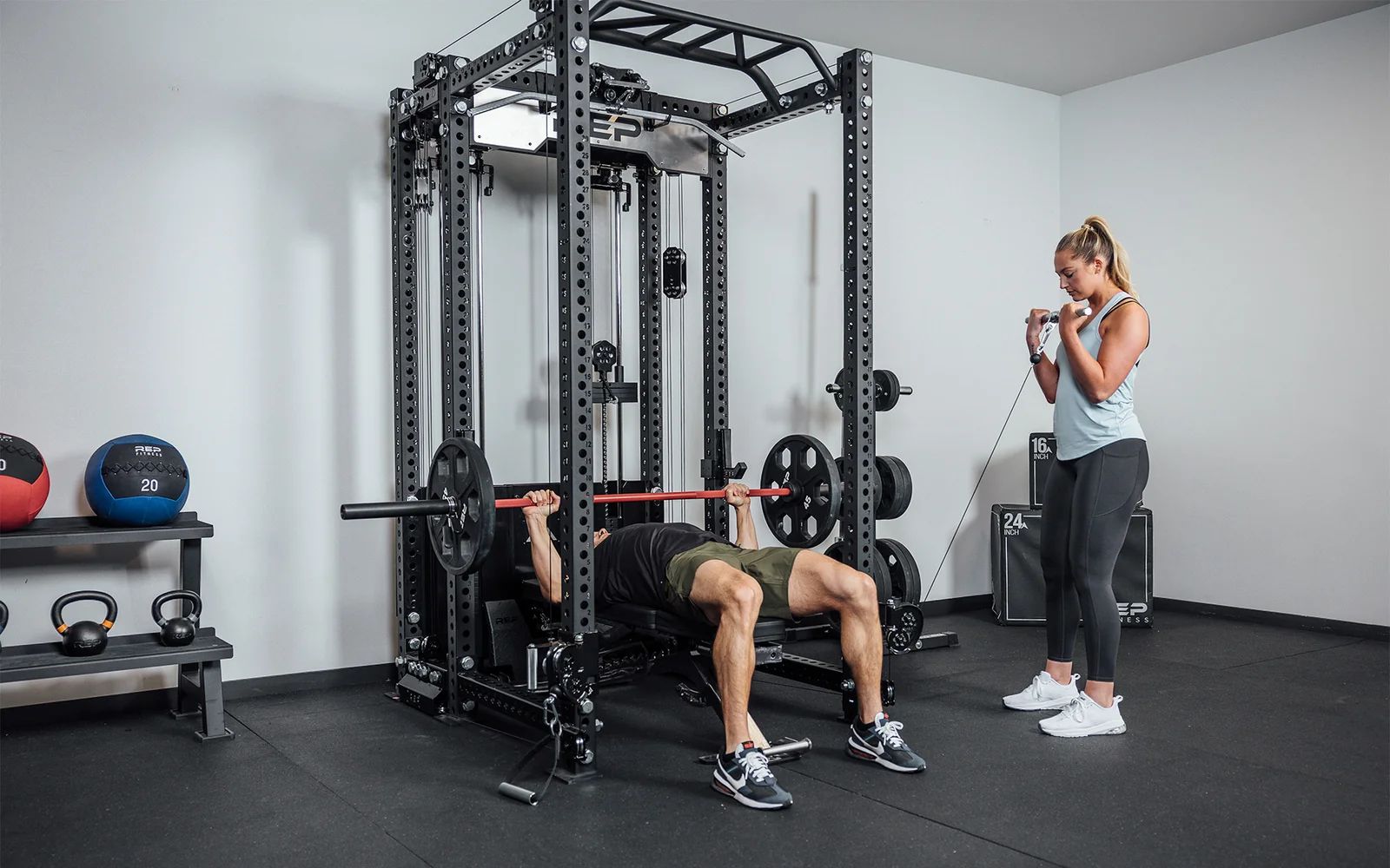 Man bench pressing inside the rack while a woman uses the side cable